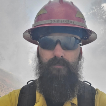 Man in hard hat with smoke in background.