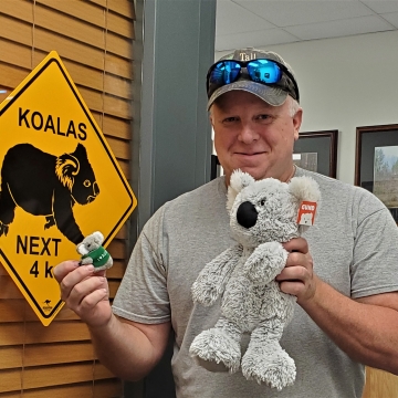 A man holding a stuffed koala in front of a sign.