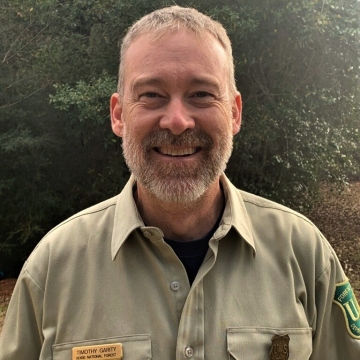 A picture of a man in a USFS uniform standing outside.